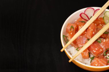 Somon ve susam, haşlanmış pirinç, taze salatalık, turp ve siyah arka plan üzerine ahşap chopcticks porselen kase yeşil soğan ile Hawaiian poke. Üstten görünüm kopya alanı ile. Organik su ürünleri