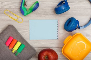 Renk modelinde çanta-kalem kalemler ve marker, elma, mavi defter, zımba, kulaklık ve öğle yemeği kutusu gri ahşap arka plan üzerinde hissetti. Üstten görünüm kopya alanı ile. Geri okul kavramı. Okul malzemeleri.