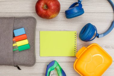 Renk modelinde çanta-kalem kalemler ve marker, elma, sarı defter, zımba, kulaklık ve öğle yemeği kutusu gri ahşap arka plan üzerinde hissetti. Üstten görünüm kopya alanı ile. Geri okul kavramı. Okul malzemeleri.