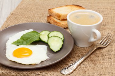 Sahanda yumurta, taze kesilmiş salatalık ve yaprak fesleğen, çatal, fincan sade kahve ve tost çul ile kaplı tablo ile plaka