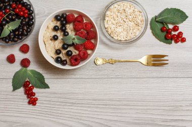 Frenk üzümü çilek ve ahududu, porselen kase yulaf lapası nane yaprakları ile süslenmiş. Cam kase yulaf gevreği ve Frenk üzümü çilek metal çatal ile. Kopya alanı ile üstten görünüm