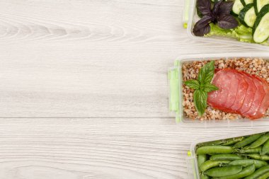 Plastik yemek kapları ile taze yeşil bezelye, haşlanmış Buğday lapası ve dilim et, salatalık ve gri arka plan üzerine salata hazırlayın. Kopya alanı ile üstten görünüm