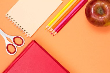 Kitap, makas, defter, renkli kalemler ve pembe bir arka plan üzerinde kırmızı elma. Üstten görünüm kopya alanı ile. Geri okul kavramı. Okul malzemeleri. Pastel renkler