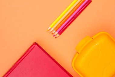 Kitap, renkli kalemler ve beslenme çantası pembe bir arka plan üzerinde. Üstten görünüm kopya alanı ile. Geri okul kavramı. Okul malzemeleri. Pastel renkler