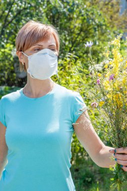 Polen alerjisi mücadele çalışıyor ve kır çiçekleri buketi tutarak koruyucu maske kadında. Onu koruyan kadın alerjenler burun. Anti kavramı.