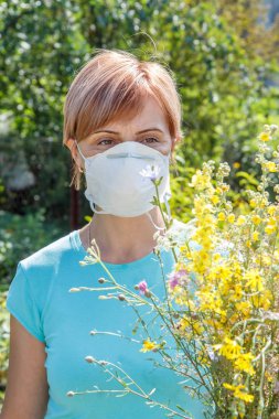 Polen alerjisi mücadele çalışıyor ve kır çiçekleri buketi tutarak koruyucu maske kadında. Onu koruyan kadın alerjenler burun. Anti kavramı.