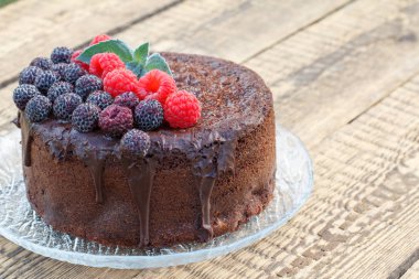 Siyah ve kırmızı ahududu cam levha ve eski ahşap kurulları ile dekore edilmiş ev yapımı çikolatalı kek