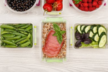 Plastik yemek kapları haşlanmış Buğday lapası ve dilim et, taze salatalık ve salata, frenk üzümü, çilek, ahududu gri arka plan üzerinde yeşil bezelye ile hazırlayın. Üstten görünüm