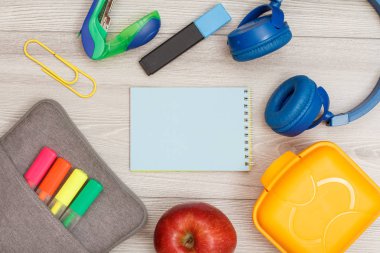 Renk modelinde çanta-kalem kalemler ve marker, elma, mavi defter, zımba, kulaklık ve öğle yemeği kutusu gri ahşap arka plan üzerinde hissetti. Üstten görünüm kopya alanı ile. Geri okul kavramı