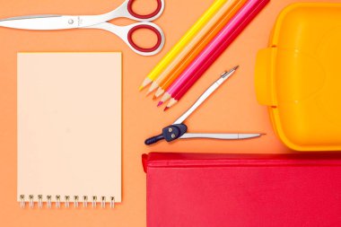 Defter, makas, renkli kalemler, pusula, pembe bir arka plan üzerinde kitap ve öğle yemeği kutusu. Üstten görünüm. Geri okul kavramı. Okul malzemeleri. Pastel renkler