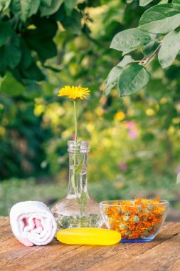 Havlu, sabun ile kadife çiçeği özü, bir cam şişeye ve kase calendula çiçeklerle doğal yeşil arka plana sahip ahşap kurullarında calendula Kuru çiçekler. Spa ürünleri ve aksesuarları