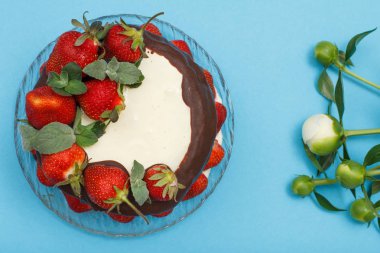 Ev yapımı çikolatalı kek taze çilek ve cam tabakta nane yaprakları ve mavi renk arka plan üzerinde peonies buket süslenmiş. Üstten görünüm