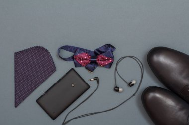 Mendil, cep telefonu, kulaklık, papyon ve gri arka plan üzerinde siyah erkek ayakkabıları. Erkekler için aksesuarlar. Kopya alanı ile üstten görünüm