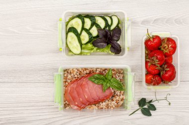 Plastik yemek kapları haşlanmış Buğday lapası ve eti, taze salatalık ve salata, gri ahşap zemin üzerine çilek dilimleri ile hazırlayın. Kopya alanı ile üstten görünüm