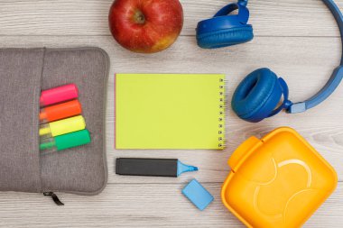 Renk modelinde çanta-kalem kalemler ve marker, elma, yeşil defter, kulaklık ve öğle yemeği kutusu gri ahşap arka plan üzerinde hissetti. Üstten görünüm kopya alanı ile. Geri okul kavramı. Okul malzemeleri.