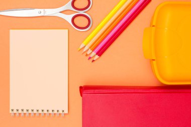 Defter, makas, renkli kalemler, pembe bir arka plan üzerinde kitap ve öğle yemeği kutusu. Üstten görünüm. Geri okul kavramı. Okul malzemeleri. Pastel renkler