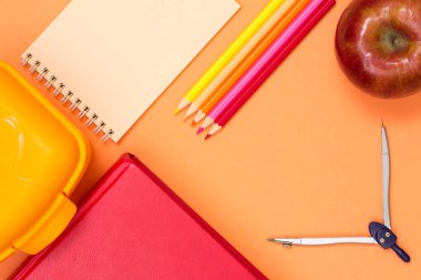 Kitap, beslenme çantası, defter, renkli kalemler, elma ve pusula pembe bir arka plan üzerinde. Üstten görünüm. Geri okul kavramı. Okul malzemeleri. Pastel renkler