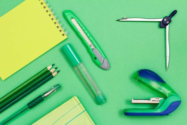 Defter, renkli kalemler, kalem, kitap, keçeli kalem, kağıt bıçak, pusula ve zımba yeşil zemin üzerine. Üstten görünüm. Geri okul kavramı. Okul malzemeleri