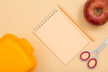 Okul malzemeleri. Beslenme çantası, defter, renkli kalem, elma ve makas bej renkli arka plan üzerinde. Üstten görünüm. Geri okul kavramı. Pastel renkler