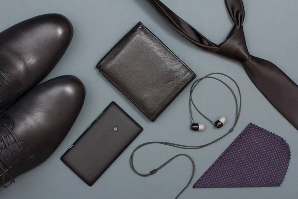 Erkek ayakkabı, deri çanta, cep telefonu, kulaklık, mendil ve kravat gri arka plan üzerine siyah. Erkekler için aksesuarlar. Üstten görünüm