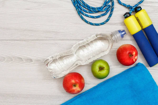 Different tools for fitness with bottle of water and apples in room or gym on grey floor