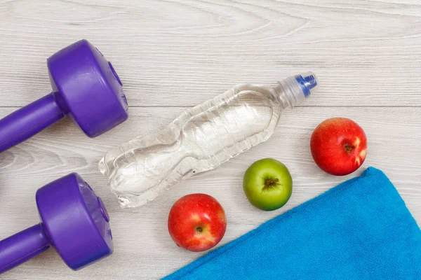 Different tools for fitness with bottle of water and apple in room or gym on grey floor