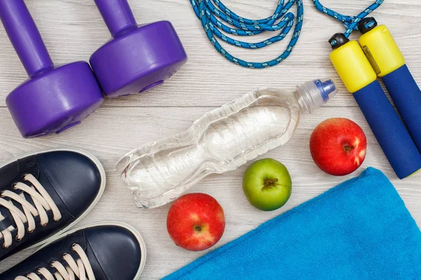 Different tools for fitness with bottle of water and apples in room or gym on grey floor