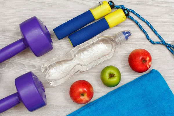 Different tools for fitness with bottle of water and apples in room or gym on grey floor