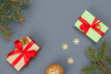 Noel dekorasyonu. Hediye kutuları, oyuncak top, dekoratif kar taneleri ve doğal köknar ağacı dalları gri arka plan üzerinde. Üstten görünüm. Noel tebrik kartı kavramı.