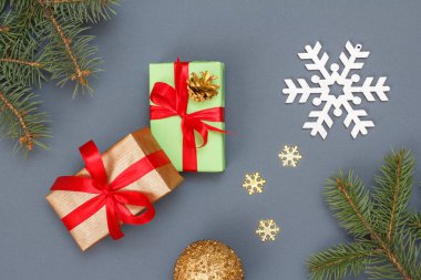 Noel dekorasyonu. Hediye kutuları, oyuncak top, dekoratif kar taneleri ve doğal köknar ağacı dalları gri arka plan üzerinde. Üstten görünüm. Noel tebrik kartı kavramı.