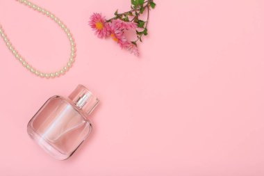 Bir şişe parfüm, boncuk ve pembe bir arka plan üzerinde çiçekler. Kadın kozmetik ve aksesuarları. Üstten görünüm.