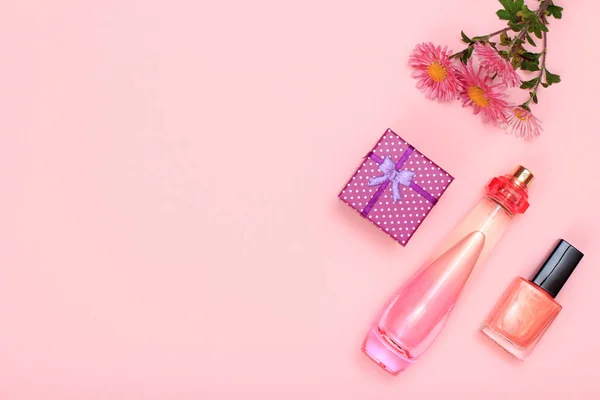 Gift box, flowers, bottle of perfume and bottle with nail polish on a pink background. Women cosmetics and accessories. Top view.