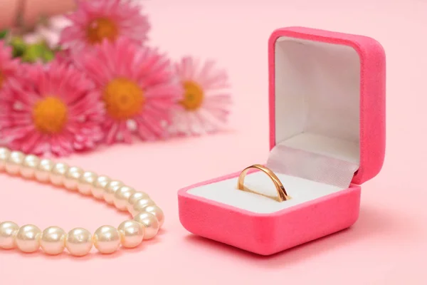 Golden ring in box, beads and flowers on a pink background. Women jewelry and accessories.