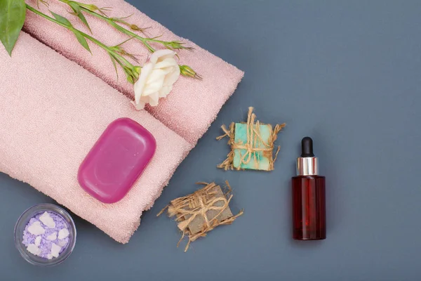 Spa products for facial and body care. Natural sea salt, homemade soap, bottle of aromatic oil and pink towels with flowers on gray background. Spa and bodycare concept. Top view.