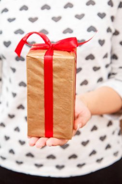 Elinde kırmızı kurdeleyle hediye kutusu tutan bir kadın. Sığ alan derinliği, seçmeli olarak kutuya odaklan. Tatilde ya da doğum gününde hediye verme kavramı.