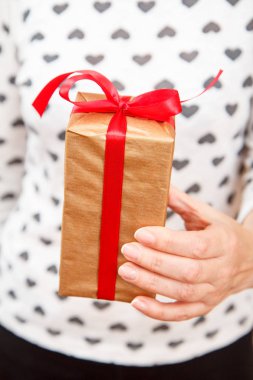 Elinde kırmızı kurdeleyle hediye kutusu tutan bir kadın. Sığ alan derinliği, seçmeli olarak kutuya odaklan. Tatilde ya da doğum gününde hediye verme kavramı.