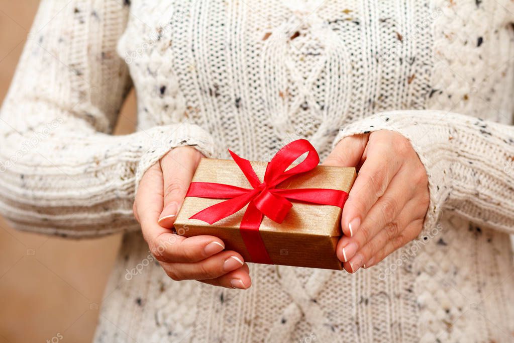 Woman holding a gift box tied with a red ribbon in her hands. Shallow depth of field, Selective focus on the box. Concept of giving a gift on holiday or birthday.