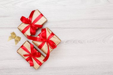 Üç hediye kutuları gri ahşap arka plan üzerinde kırmızı kurdele ile bağlanmış. Kopya alanı ile üstten görünüm.