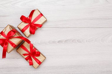 Üç hediye kutuları gri ahşap arka plan üzerinde kırmızı kurdele ile bağlanmış. Hediyeler vererek kavramı. Kopya alanı ile üstten görünüm.