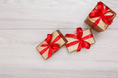 Üç hediye kutuları gri ahşap arka plan üzerinde kırmızı kurdele ile bağlanmış. Hediyeler vererek kavramı. Kopya alanı ile üstten görünüm.