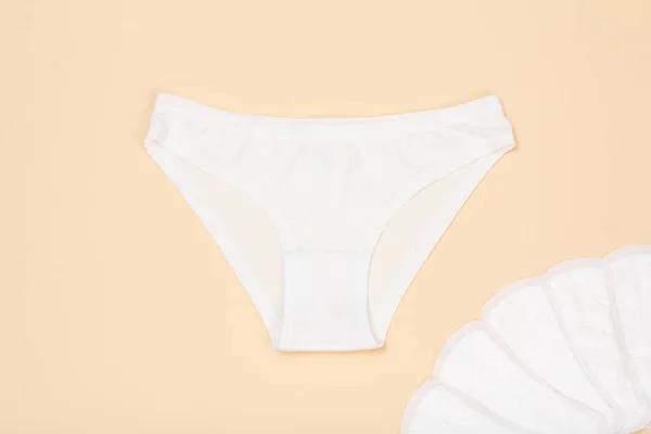 Beautiful panties with sanitary napkins on beige background. Women underwear set. Top view.