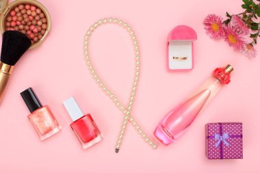Hediye kutusu, boncuk, şişe parfüm, tırnak cilası ve kutusunda, toz pembe bir arka plan üzerinde fırça ile altın yüzük. Kadın kozmetik ve aksesuarları. Üstten görünüm.