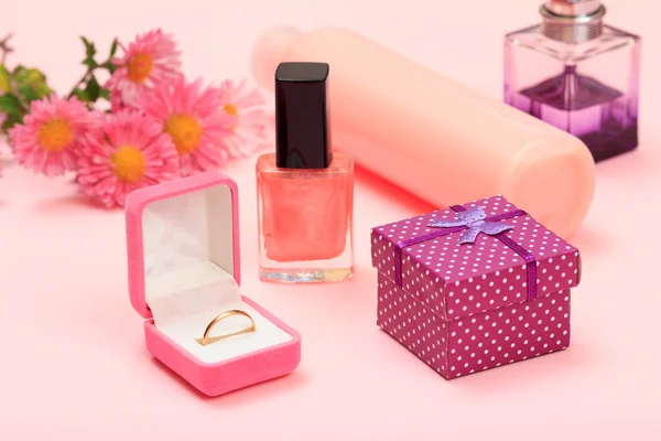 Gift box, flowers, bottles with nail polish, shampoo and perfume, golden ring in a box on a pink background. Women cosmetics and accessories.