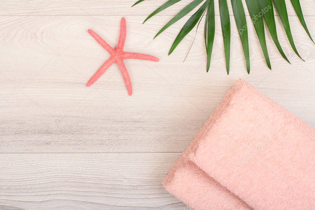 Stack of soft terry towels with sea star and green leaf on wooden background. Spa products. Top view.