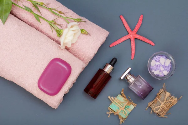 Spa products for facial and body care. Natural sea salt, homemade soap, aromatic oil, perfume and pink towels with flower and sea star on gray background. Spa and bodycare concept. Top view.