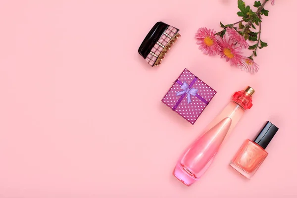 Gift box, hairgrip, flowers, bottle of perfume and bottle with nail polish on a pink background. Women cosmetics and accessories. Top view with copy space..