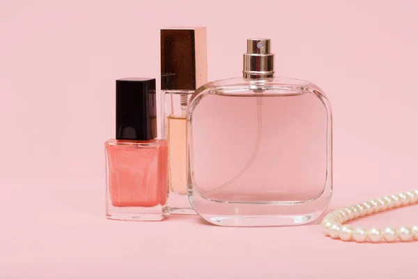 Bottles with women perfumes, nail polish and beads on a string in a pink background. Women cosmetics and accessories.