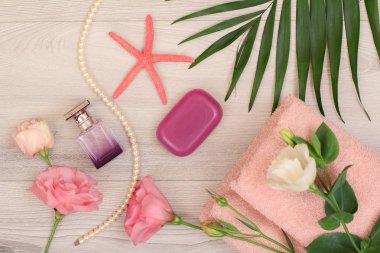 Pembe çiçekler, sabun, şişe parfüm, deniz yıldızı ve yeşil ile yumuşak terry havlu yığını ahşap arka plan üzerinde bırakır. Spa ürünleri. Üstten görünüm.