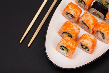 Uramaki California. Suşi rulo nori, pirinç, adet avokado, salatalık, ahşap sopa ile seramik plaka üzerinde uçan balık karaca ile dekore edilmiştir. Üstten görünüm.