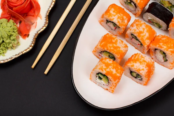 Uramaki California. Suşi rulo nori, pirinç, adet avokado, salatalık, ahşap sopa ile seramik plaka üzerinde uçan balık karaca ile dekore edilmiştir. Kırmızı Turşu Zencefil ve wasabi ile plaka. Üstten görünüm.